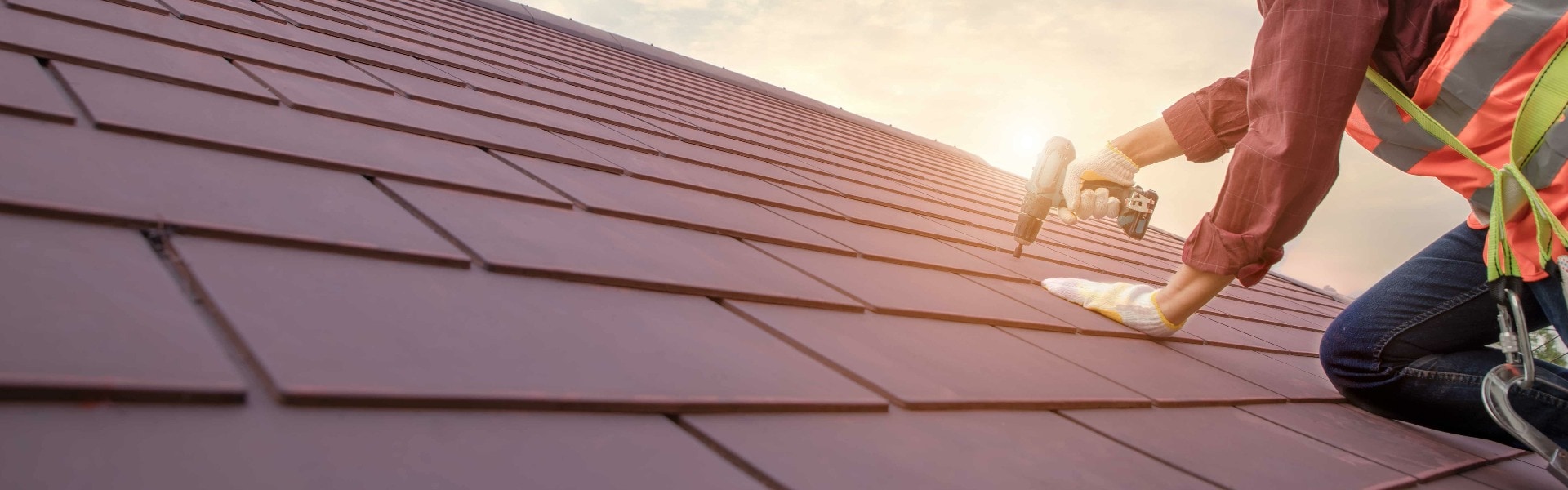 Roofer working in special protective work wear gloves, using air or pneumatic nail gun installing concrete or CPAC cement roofing tiles on top of the new roof under construction residential building